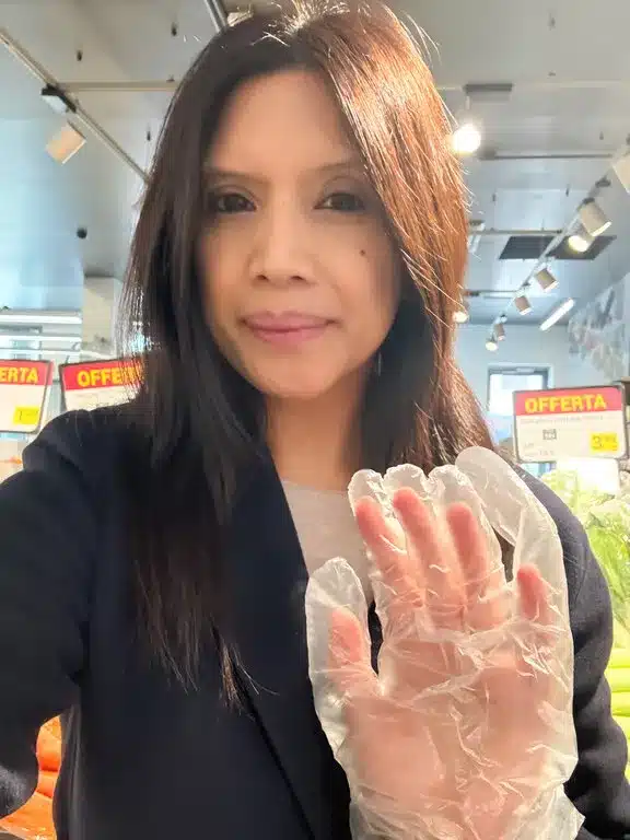 Lisa Rivera wearing a mandatory disposable plastic glove while selecting fresh produce in an Italian supermarket fruit and vegetable section