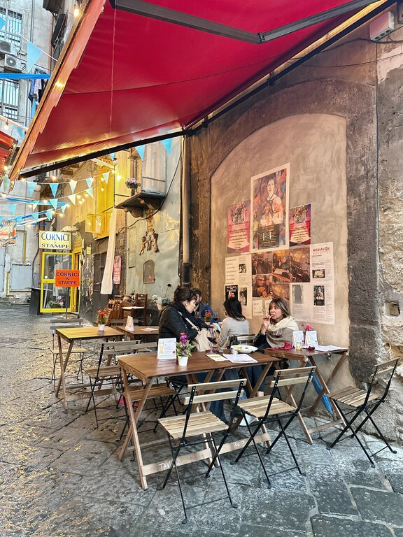 People sitting at a traditional outdoor cafe in the narrow streets of Quartiere Spagnoli, Naples, Italy