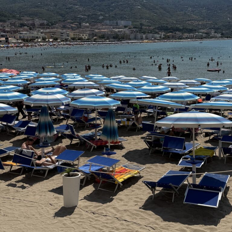 Row of blue and white striped beach umbrellas on the sandy shore of Cefalu, Sicily during a sunny August afternoon