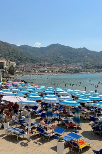 A row of colorful beach umbrellas on the sand at Porto Vecchio in Cefalù, Sicily, famously featured as the White Lotus beach location