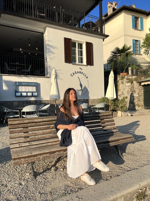 Lisa Rivera sitting on a bench in Isola Bella, Piedmont, wearing a blue shawl over a long white dress