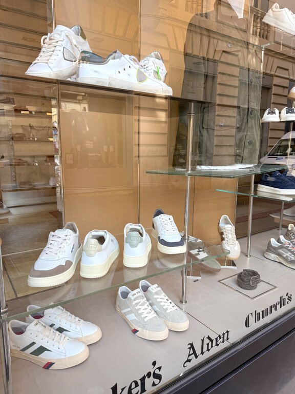Selection of men's white sneakers from different brands displayed in an Italian shop window. Photo taken by Lisa Rivera