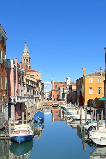 A canal lined with boats and with blue skies in February in Italy