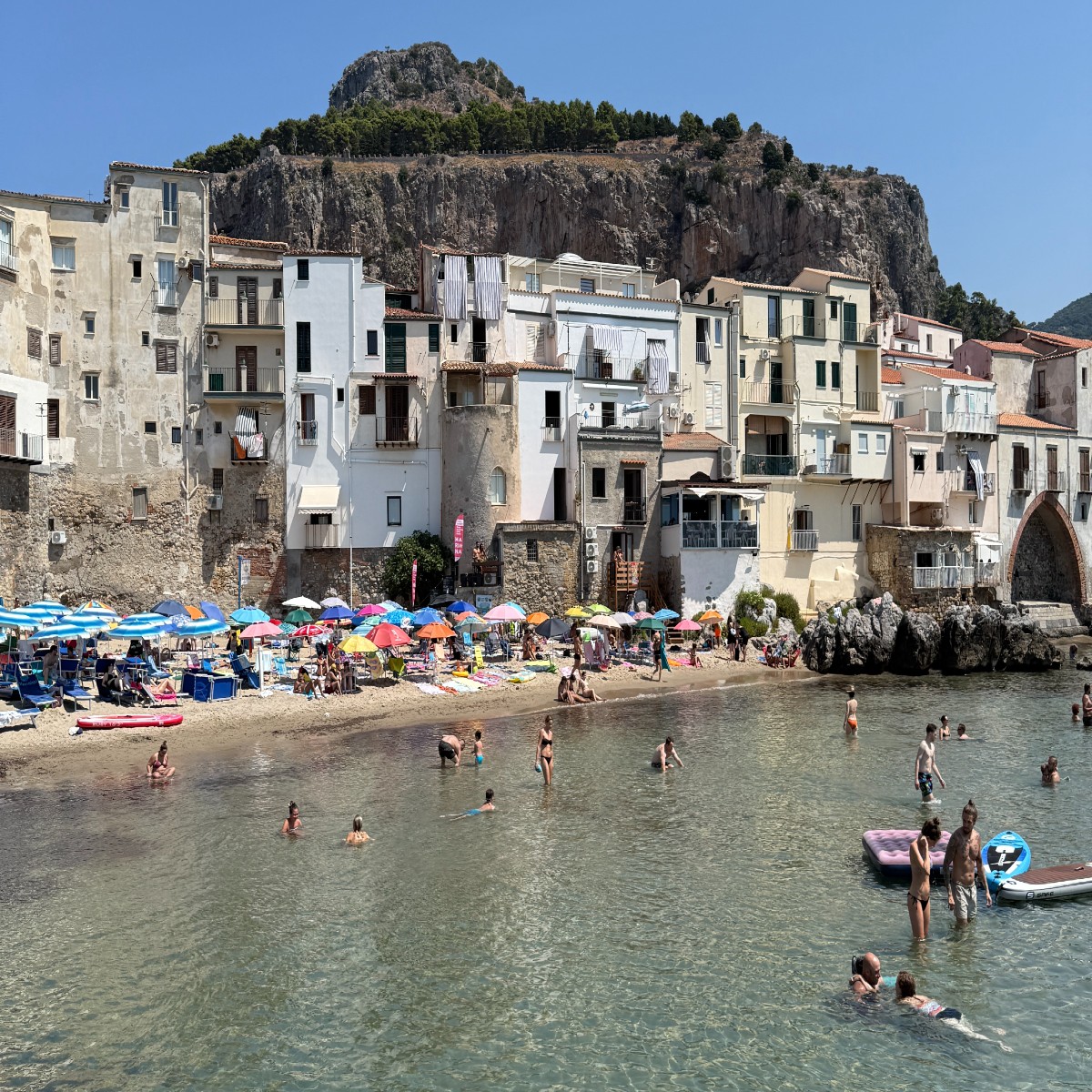 People relaxing on the sandy beach and swimming in the sea at Cefalù