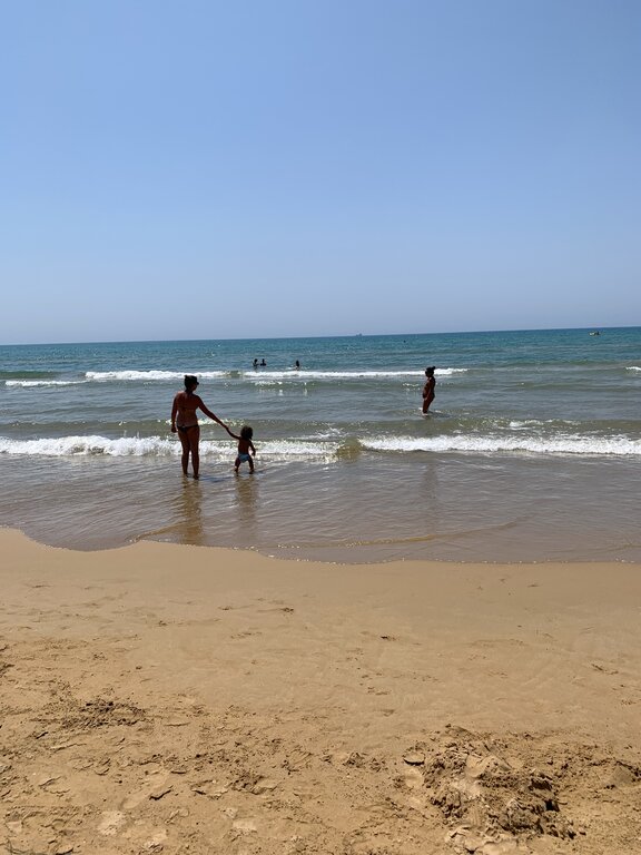 A mother and toddler playing at the water's edge at Santa Maria del Focallo beach in southern Sicily, one of the best family-friendly beaches on the island